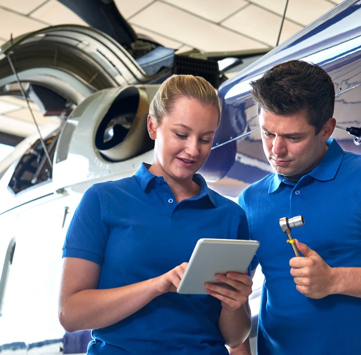 Uma mulher e um homem olhando para um tablet, com um avião ao fundo