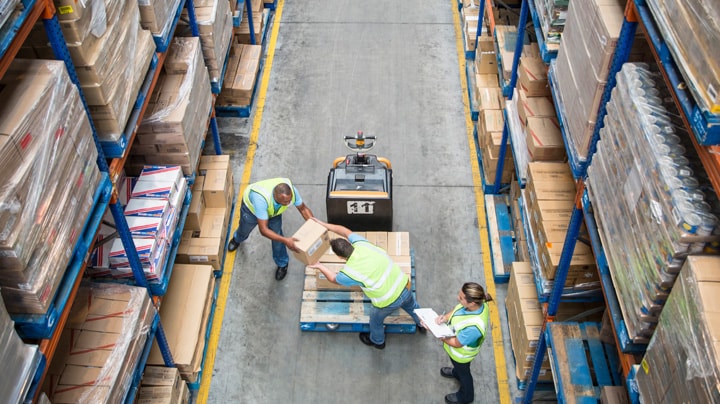 Trois personnes empilant des cartons sur un transpalette