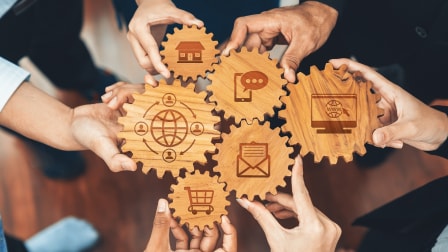 Persons holding interconnected wooden gears engraved with business and communication icons.Multiple hands holding interconnected wooden gears engraved with business and communication icons
