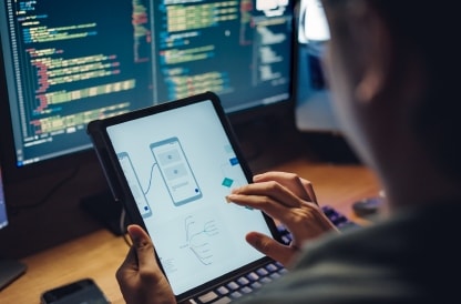 Developer reviewing a mobile app design on a tablet in front of code monitors