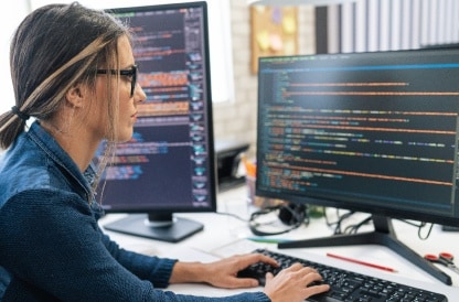 Woman coding on multiple computer monitors
