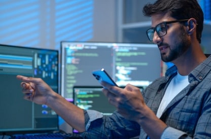 Developer testing code on a smartphone in front of monitors