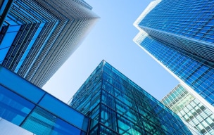 Homem de negócios em um terno segurando um smartphone enquanto está perto de uma janela em um escritório moderno