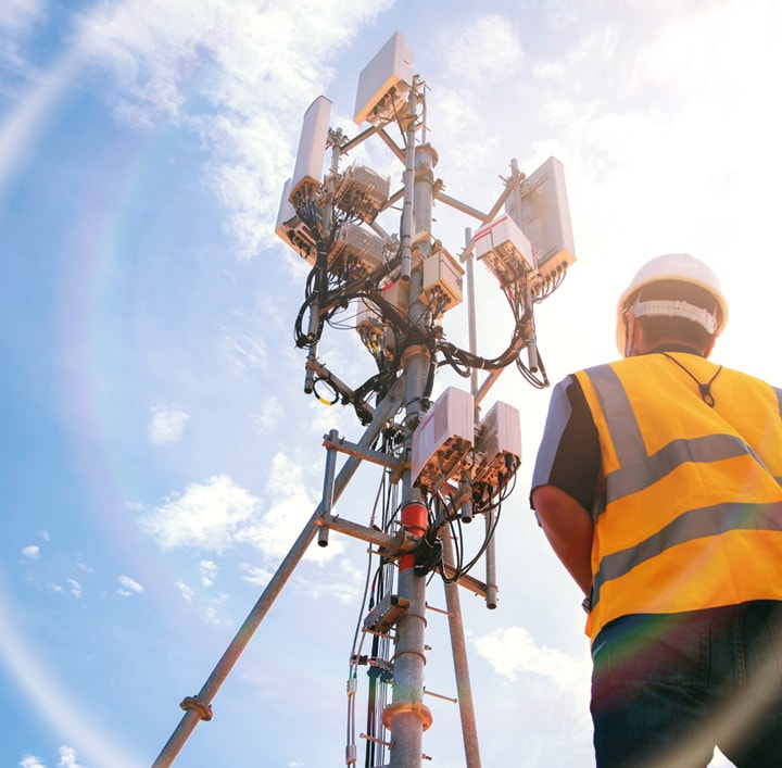 man in safety vest and hard hat facing network communications pole