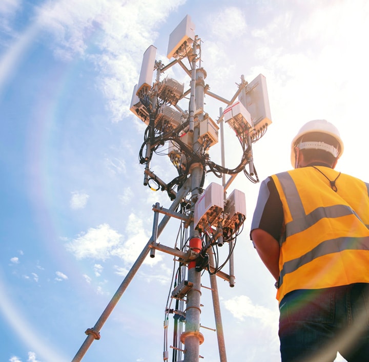 uomo con giubbotto di sicurezza e elmetto rivolto verso il palo delle comunicazioni di rete