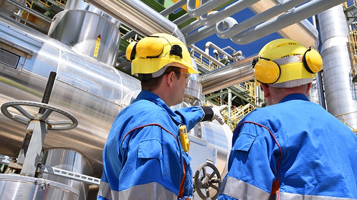 Two men wearing yellow hard hats navigating energy equipment