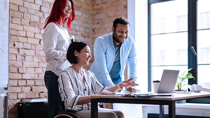 Three people looking at a laptop in an office