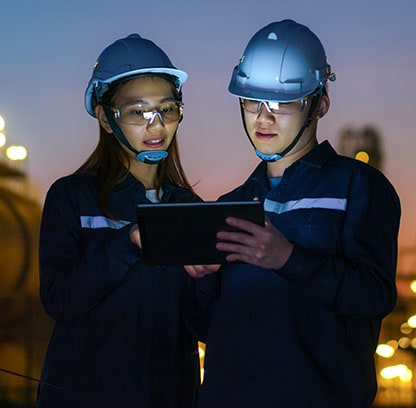 Two workers with helmets and safety glasses on looking at a tablet in the early morning