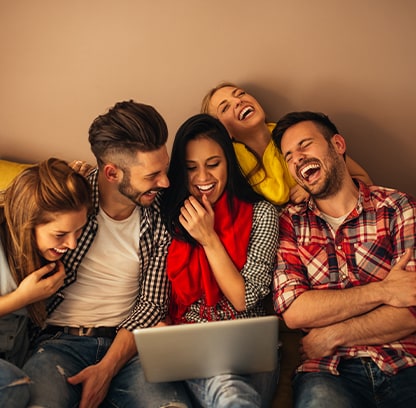 Eine Gruppe von lachenden Menschen sitzt auf einer Couch und blickt auf einen Laptop