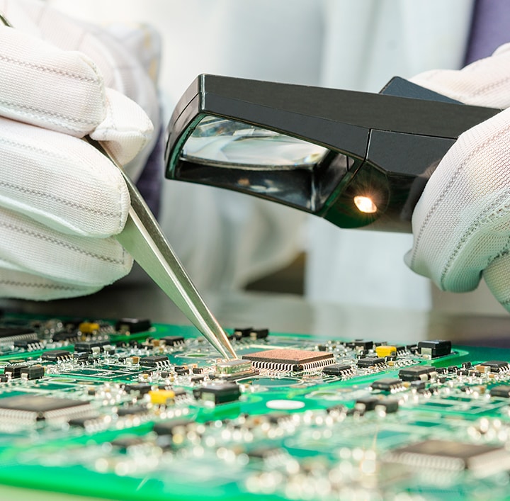 Hands wearing gloves working on computer hardware with magnifying glass