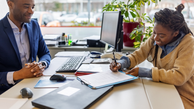 A person signing documents at a desk with an advisor