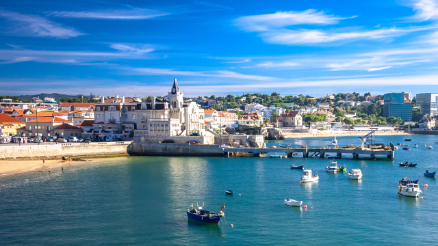 Coastal town with colorful buildings, a small harbor, and boats on calm blue water.