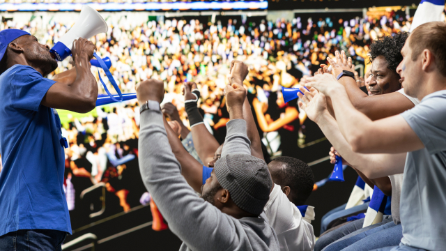 Excited crowd of sports fans cheering with raised hands at a packed stadium