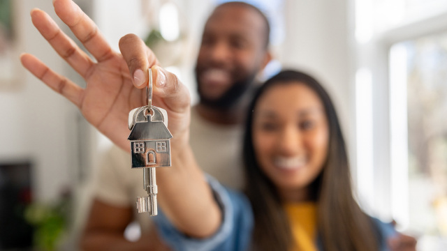 Couple holding up house keys, smiling in the background