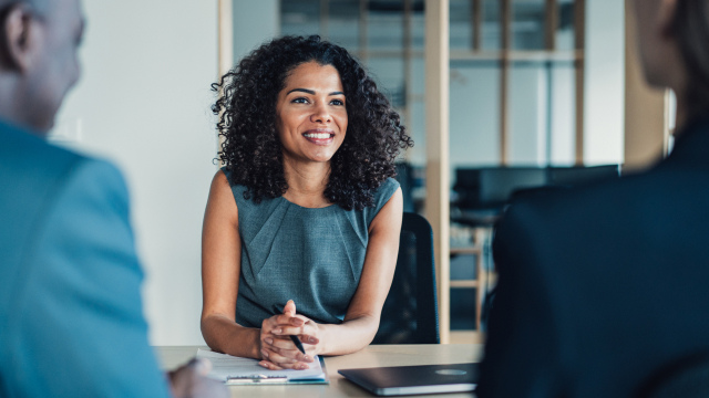 Smiling woman sitting at a desk in a meeting, engaged in conversation