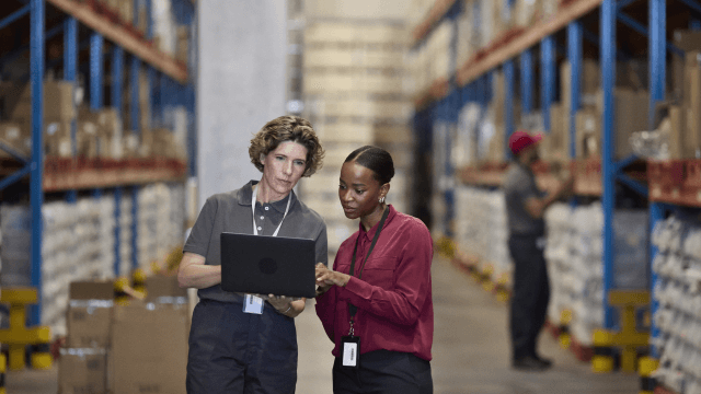 Two warehouse employees using a laptop for inventory management in a logistics facility