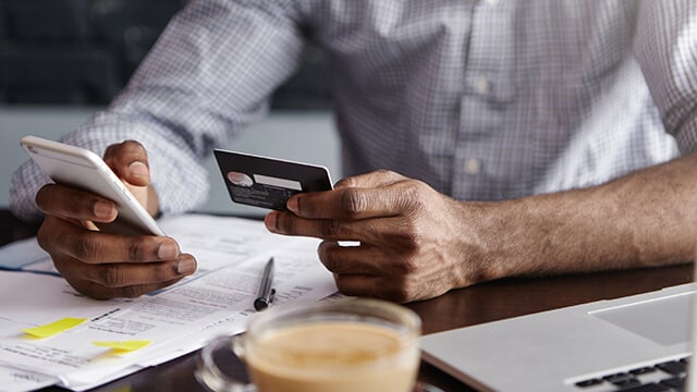 Person holding and looking at a credit card and a cellphone in each hand.