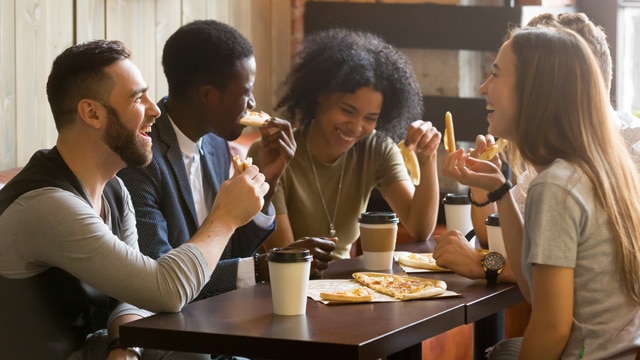 People laughing and eating pizza at a table.