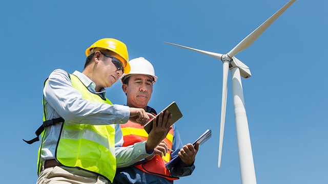 colleagues working on tablets with wind turbine in background