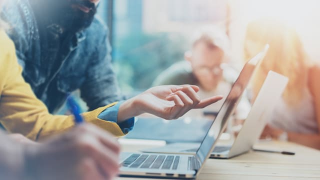 People sitting at a desk pointing at a laptop.