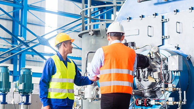 Two workers wearing hard hats and safety vests in manufacturing facility