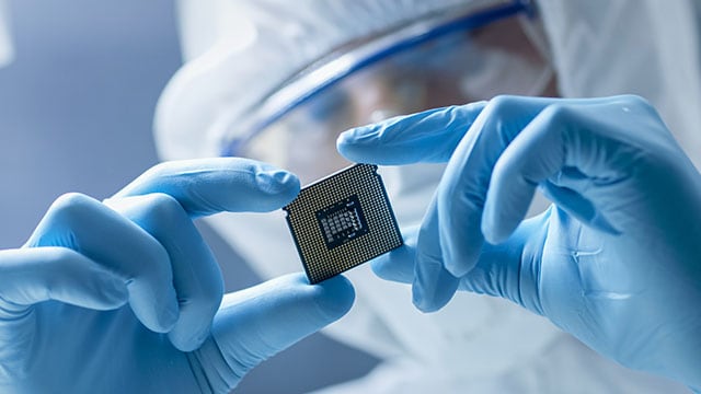 Technician in protective suit and gloves looking at computer chip