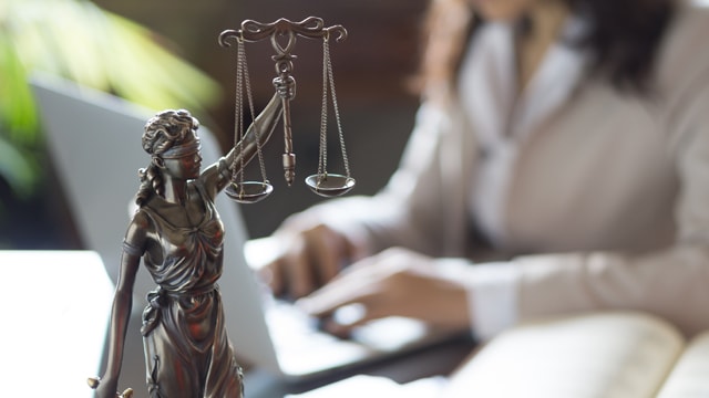 Woman working on laptop with scales of justice in foreground