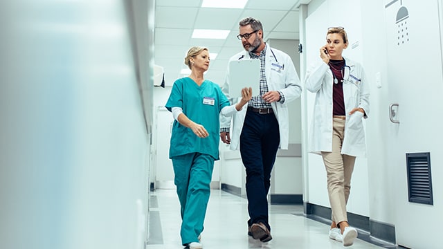 Medical professionals walking down hallway discussing file.