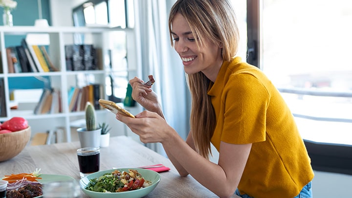 Young woman checking her device while eating a salad