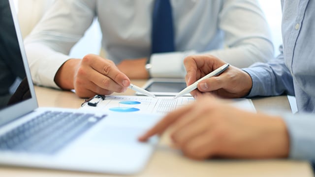 People looking at financial papers with laptop on desk.