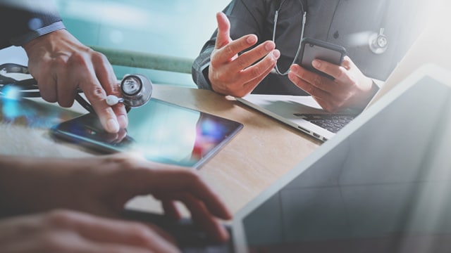 Doctors having a discussion at a table using tablets and laptops