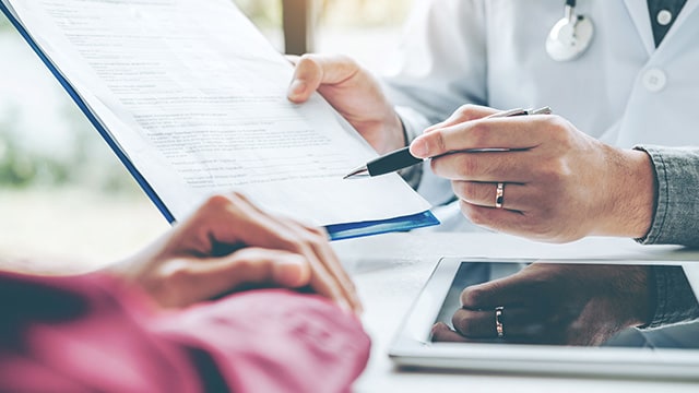 A doctor pointing to something on a clipboard to someone else.