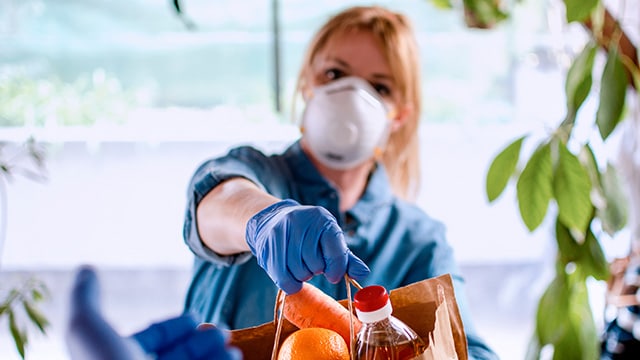 Women holding a bag of groceries while wearing gloves and a mask.
