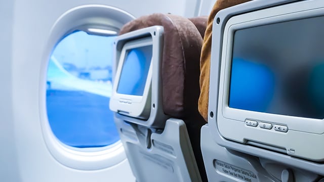 Back of airplane seats with screens on headrests.