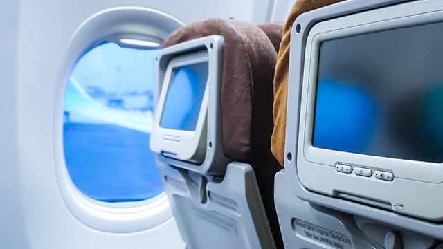 Back of airplane seats with screens on headrests.