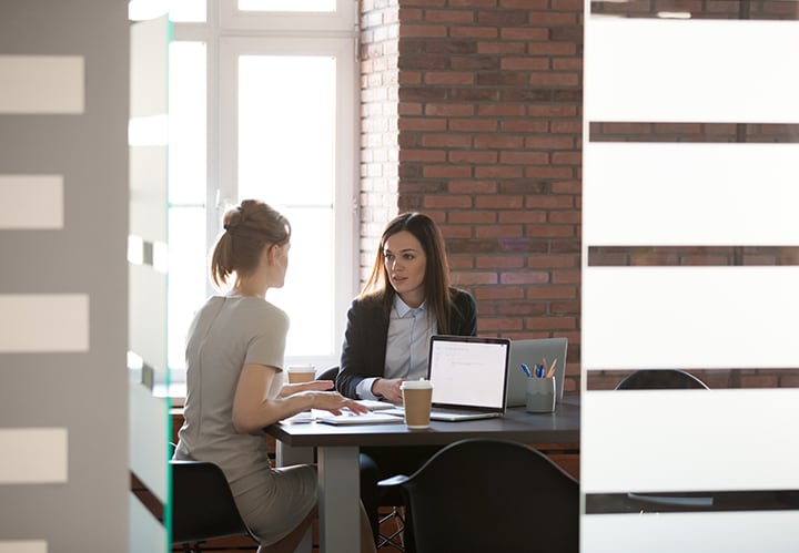 Two women having a discussion while working on laptops in a meeting room