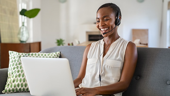 Frau sitzt mit Laptop auf der Couch und spricht über ein Headset