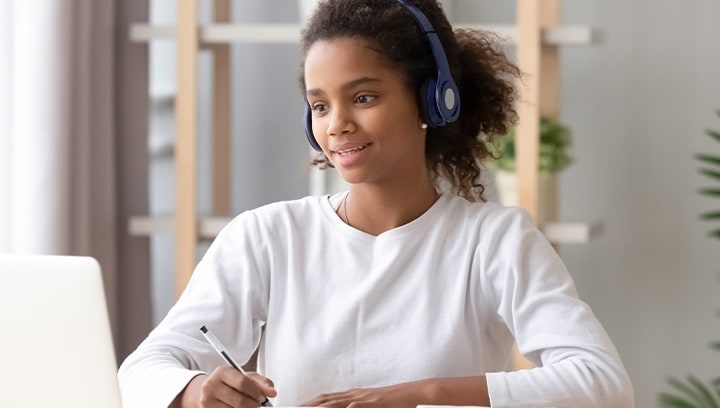 Frau mit Headset sitzt am Schreibtisch und schaut auf den Laptop