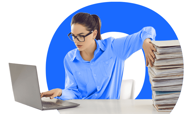 Woman managing a stack of files on her desk while working on a computer