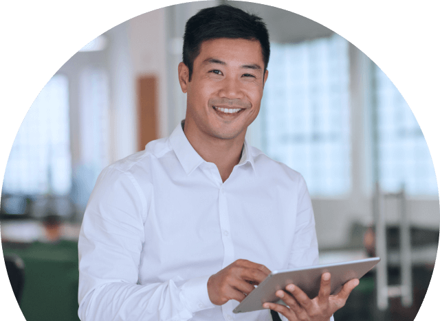 A person smiling in an office, holding a tablet.