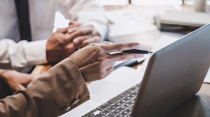 Hand pointing at laptop describing something to someone in the office